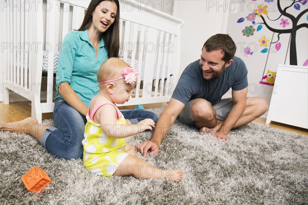 Mid adult couple playing with baby daughter on nursery rug