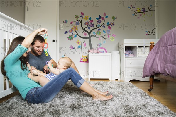 Mid adult couple playing with baby toy and baby daughter on lap