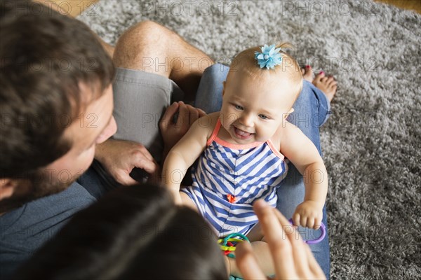 High angle view of mid adult couple playing with baby daughter on lap