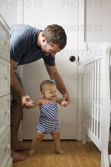 Mid adult man holding baby daughter hands whilst toddling in nursery