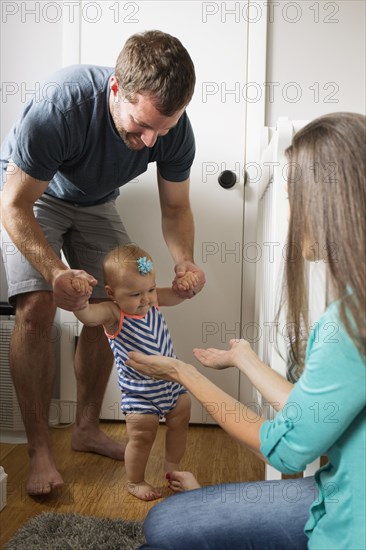 Mid adult man holding unsteady baby daughter hands whilst toddling in nursery