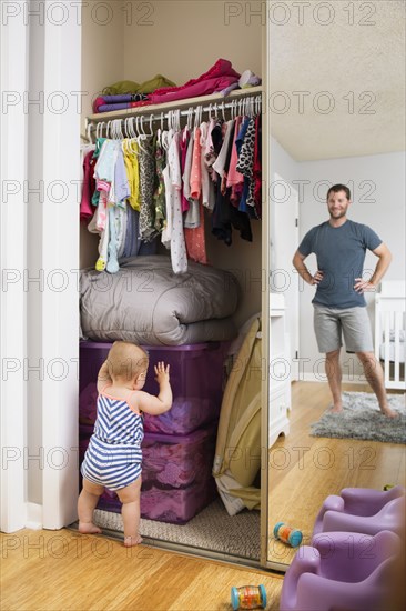 Mid adult man watching baby daughter search box in wardrobe