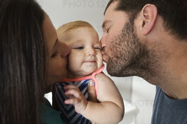 Close up of mid adult couple kissing baby daughter on each cheek