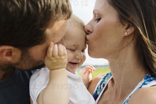 Close up of mid adult parents kissing baby daughter