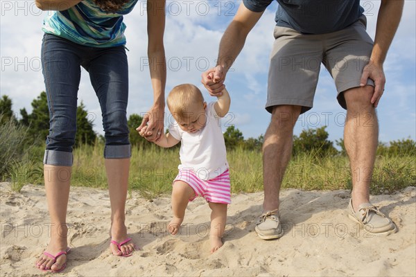 Mid adult parents holding baby daughters hands while toddling in sand