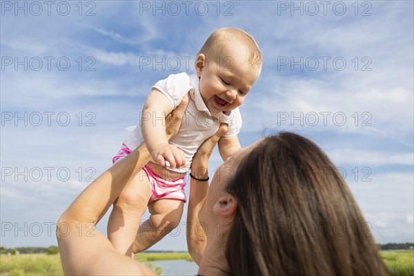 Mid adult woman holding up baby daughter on riverside