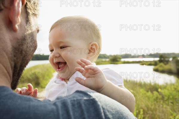 Over shoulder view of mid adult man carrying baby daughter on riverside