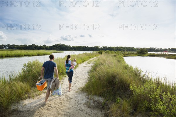 Rear view of mid adult parents carrying baby daughter on riverside picnic