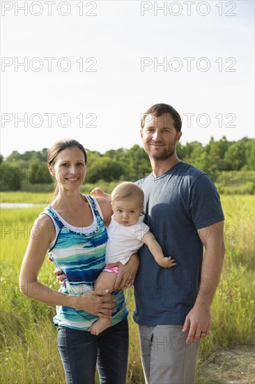 Portrait of mid adult parents carrying baby daughter by rural field