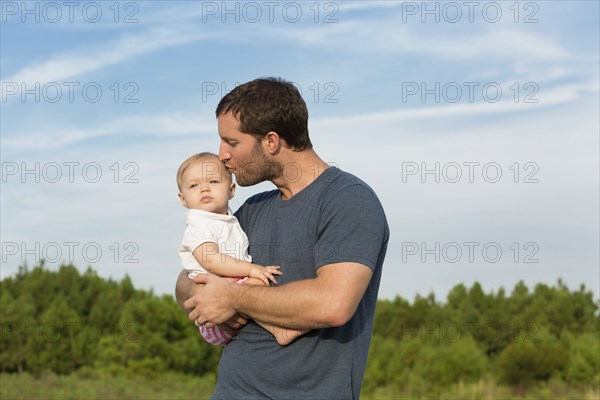 Mid adult man kissing baby daughter on cheek in rural outdoor