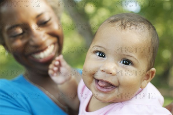 Head and shoulders of mother holding baby girl looking at camera smiling