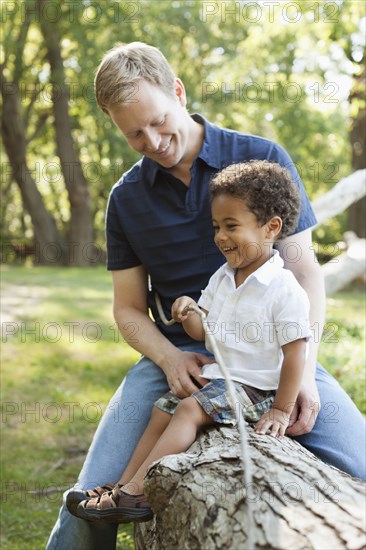 Father and son sitting on log holding twig smiling