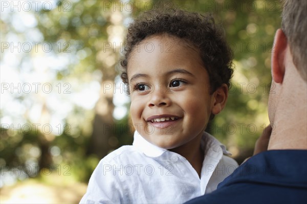 Over shoulder view of father carrying preschool boy looking away smiling