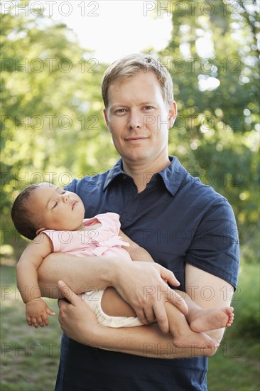 Father outdoors holding baby girl looking at camera smiling