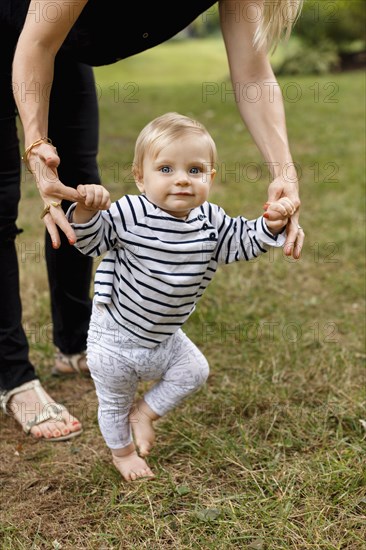 Mother holding baby girl's hands to help her walk