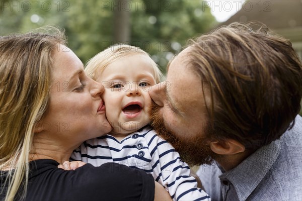 Mother and father kissing baby girl on cheek