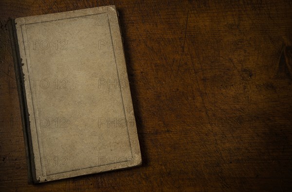 Old book with blank cover resting on old wooden desk top