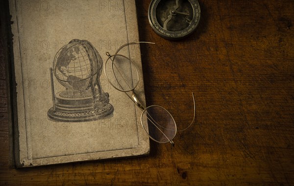 Old book resting on old wooden desk top with old eyeglasses and small sundial