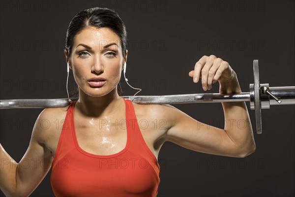 Studio portrait of athletic woman in red sleeveless top with barbell