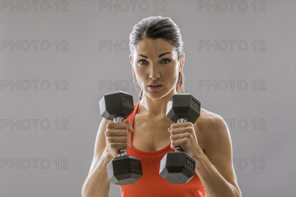 Studio portrait of athletic woman in red sleeveless top with dumbbells