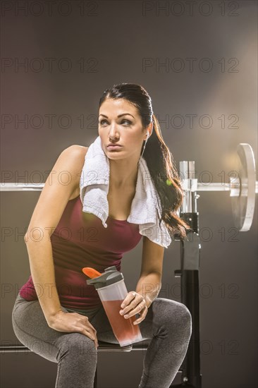 Studio shot of woman in sleeveless top sitting at barbell