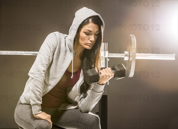 Studio shot of woman in hooded shirt exercising with dumbbell