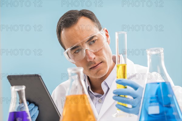 Scientist with digital tablet looking at yellow liquid in beaker