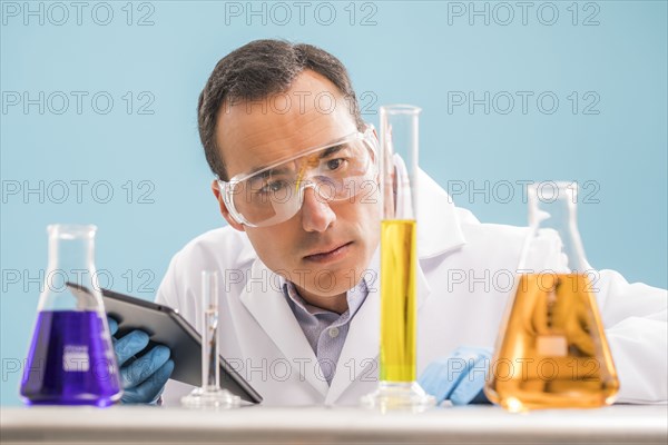 Scientist with digital tablet looking at yellow liquid in measuring beaker