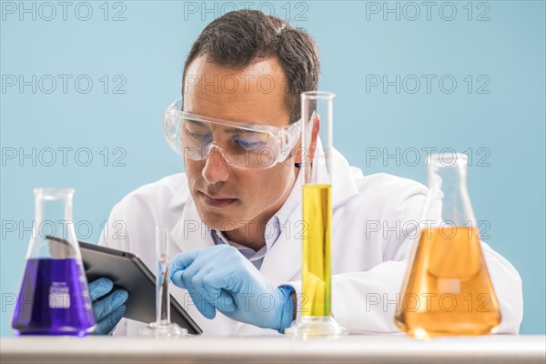 Scientist with digital tablet looking at yellow liquid in measuring beaker