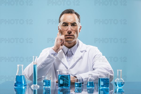 Portrait of scientist with beakers with blue liquid in foreground