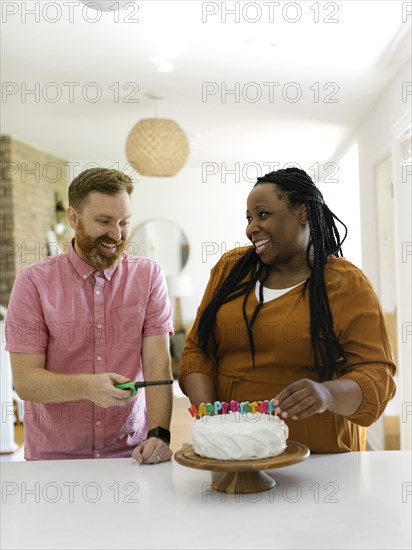 Smiling couple lighting birthday candles on cake