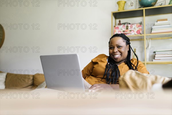 Smiling woman sitting on sofa and working on laptop