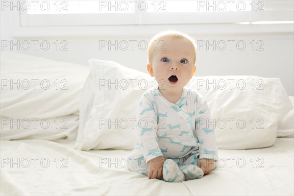 Baby boy with open mouth sitting on bed