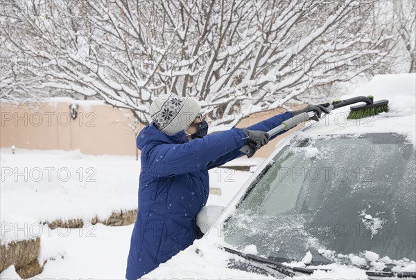 Woman in face mask removing snow from car