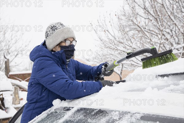 Woman in face mask removing snow from car