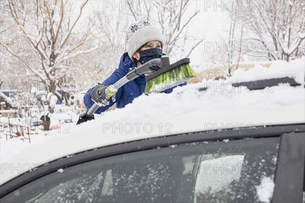 Woman in face mask removing snow from car