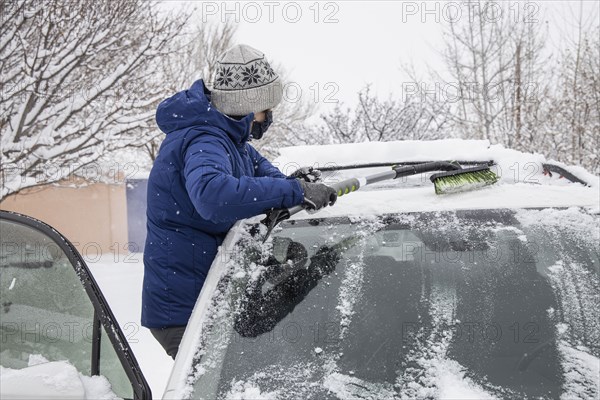 Woman in face mask removing snow from car