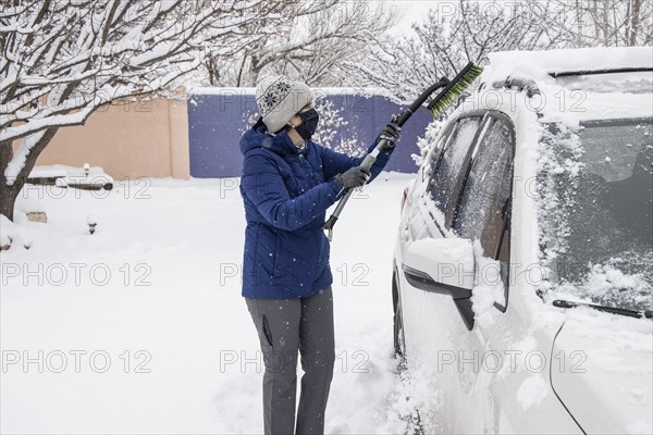 Woman in face mask removing snow from car