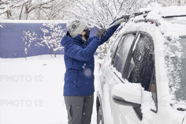 Woman in face mask removing snow from car