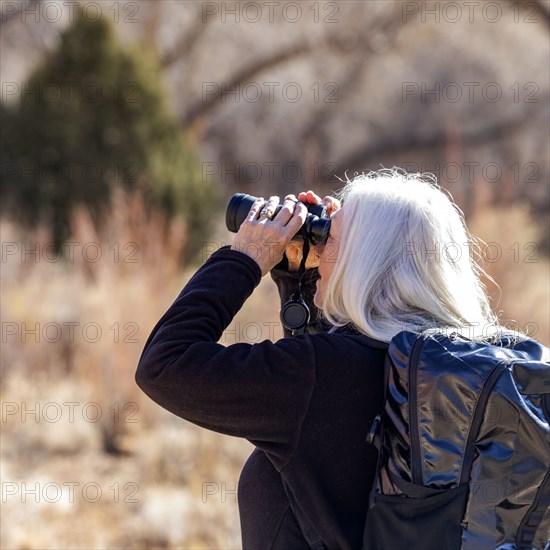 Senior woman uses binoculars while hiking