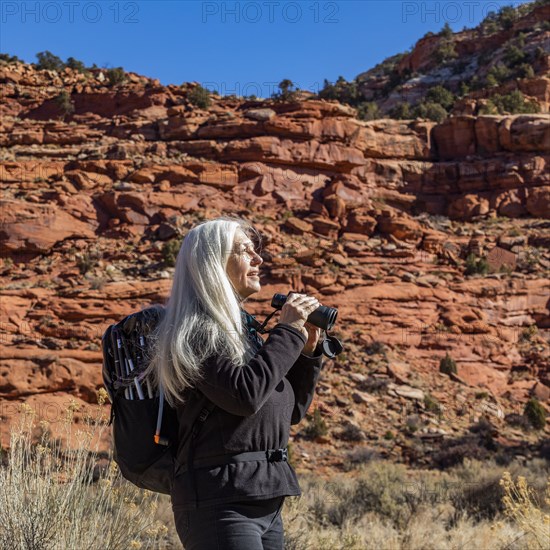 Senior woman uses binoculars while hiking in Grand Staircase-Escalante National Monument