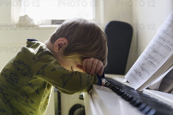 Sad boy (6-7) leaning on piano