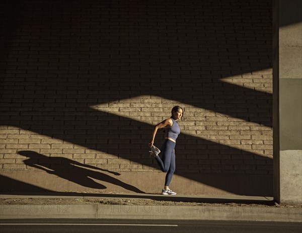 Woman stretching near brick wall in sunlight