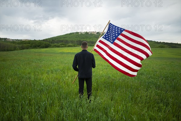 Rear view of man with American flag in wheat field