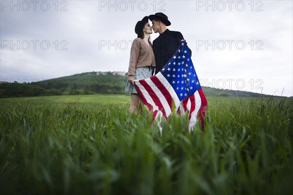 Young couple with American flag kissing in wheat field