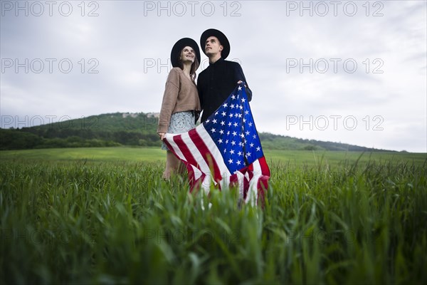 Young couple holding American flag in wheat field