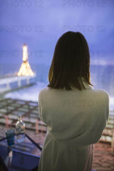 Rear view of woman in bathrobe in hotel with view on sea at night