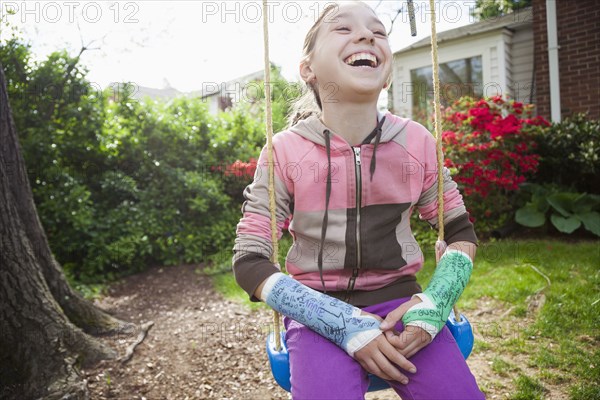 Smiling girl (12-13) with two arm casts sitting in tree swing