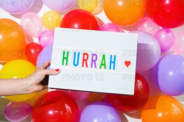 Woman holding sign saying Hurrah in front of balloon wall