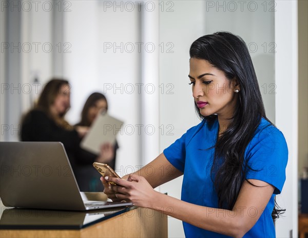Female doctor with smart phone and laptop at reception desk